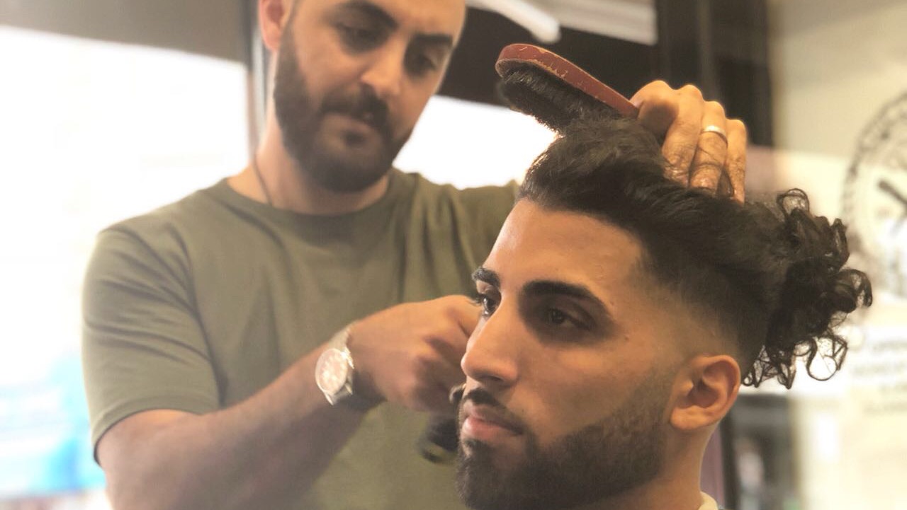 A barber at The Clip Joint combing through a client's curly top mid-cut