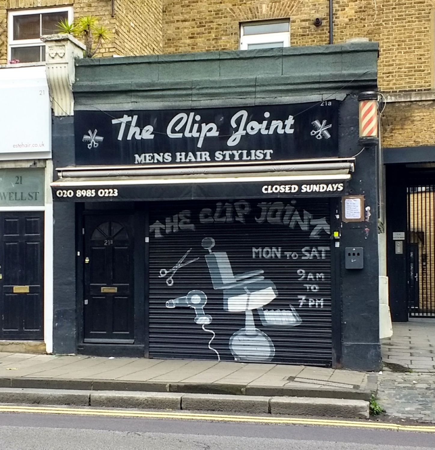 The Clip Joint shopfront on Well Street, Hackney — black fascia with the hand-painted script sign, MENS HAIR STYLIST and a red, white and blue barber pole